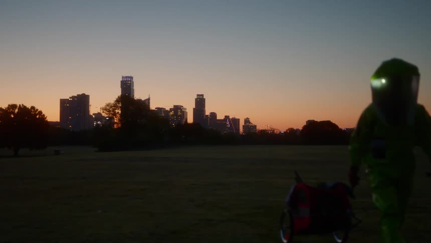 A person with a hazmat suit pulling a cart with a city skyline in the background