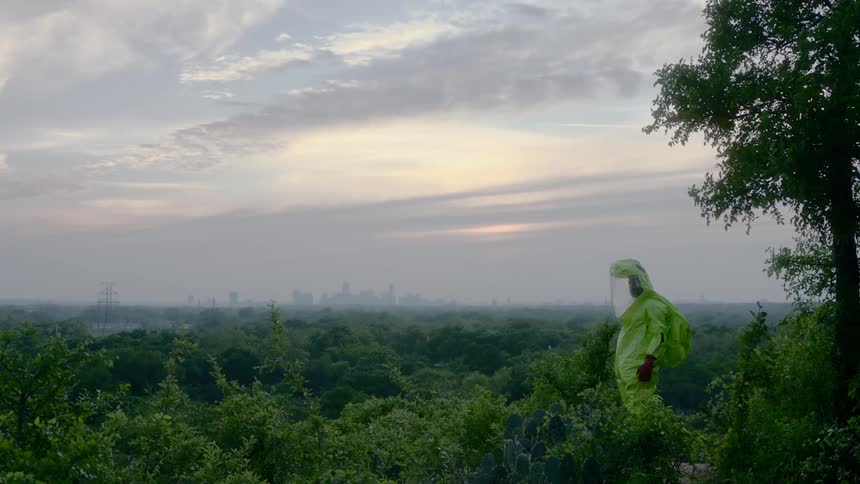 A man in a hazmat suit stands in a flower garden and looks around