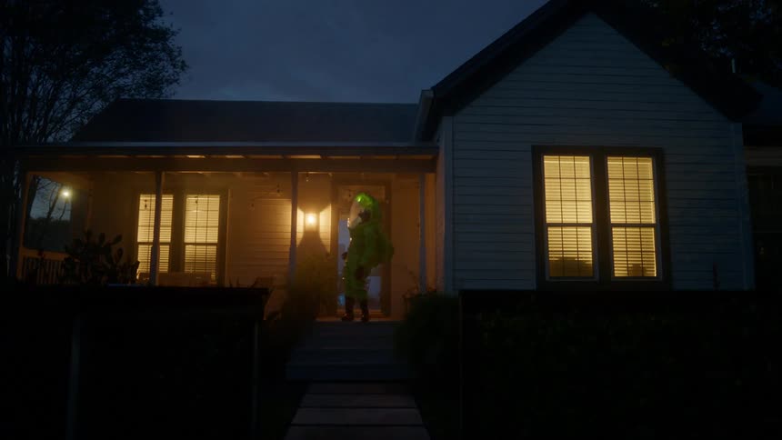 A man in a space suit stands on the porch of a house