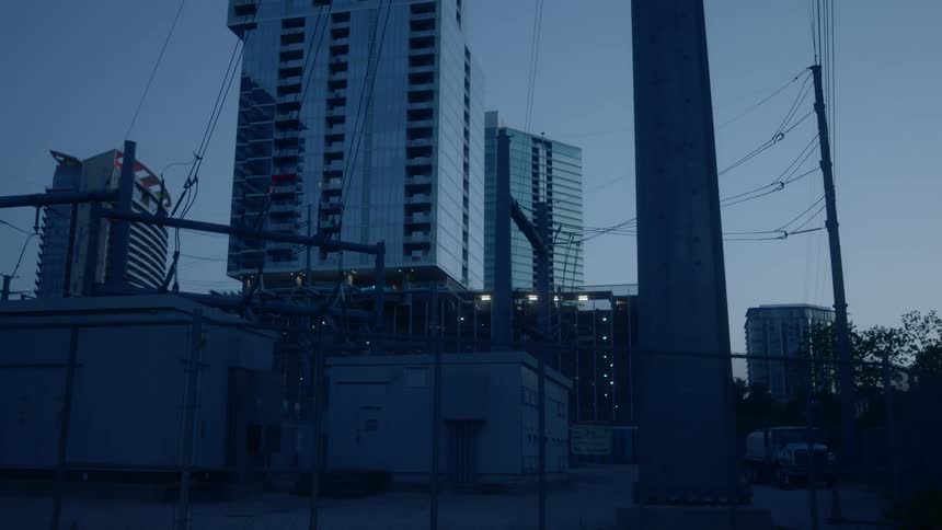 Truck occupies parking lot behind chain link fence at power station bordering skyscrapers