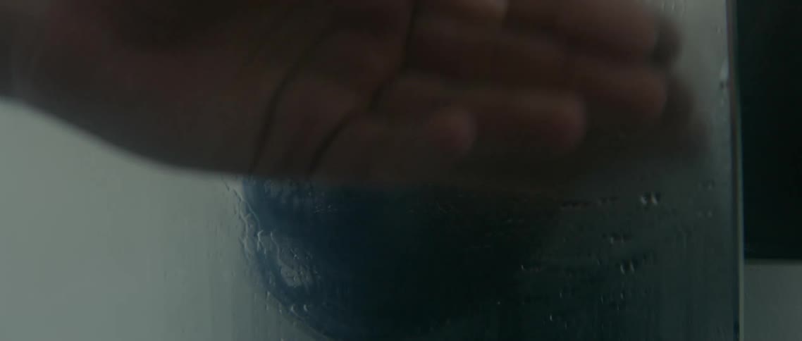 A man wearing a towel wipes the steam off a mirror with his hand