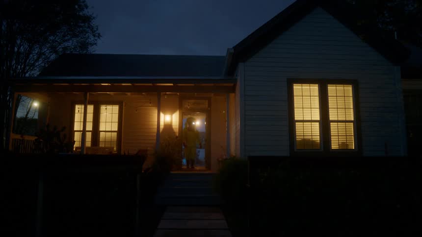 A person in a hazmat suit emerging from the front door of a house at night