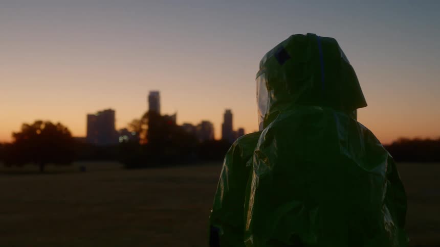 A person in a hazmat suit walks towards a city