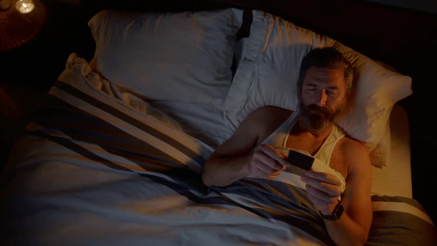 Bearded man lying on the bed looks at the photograph before sleeping in the bedroom