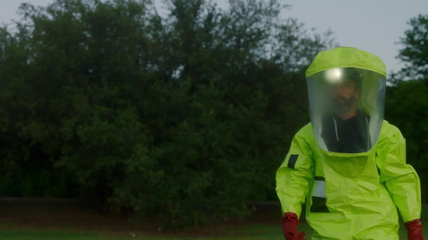 A man walking with a green hazmat suit on with trees in the background
