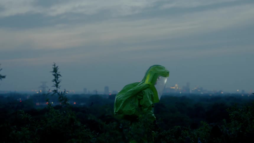 Person wearing a protective suit walks through bushes while fog obscures distant city skyline