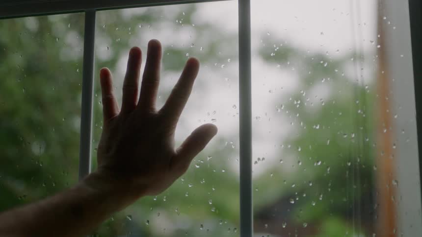 A person puts their hand against the window