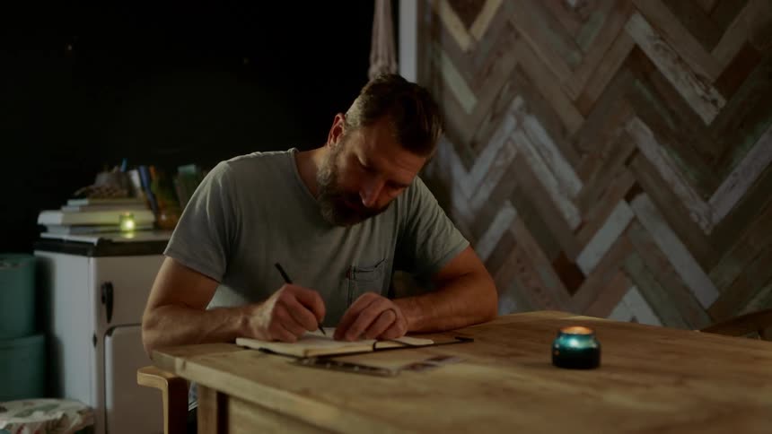 A man sits at a table and writes in a book