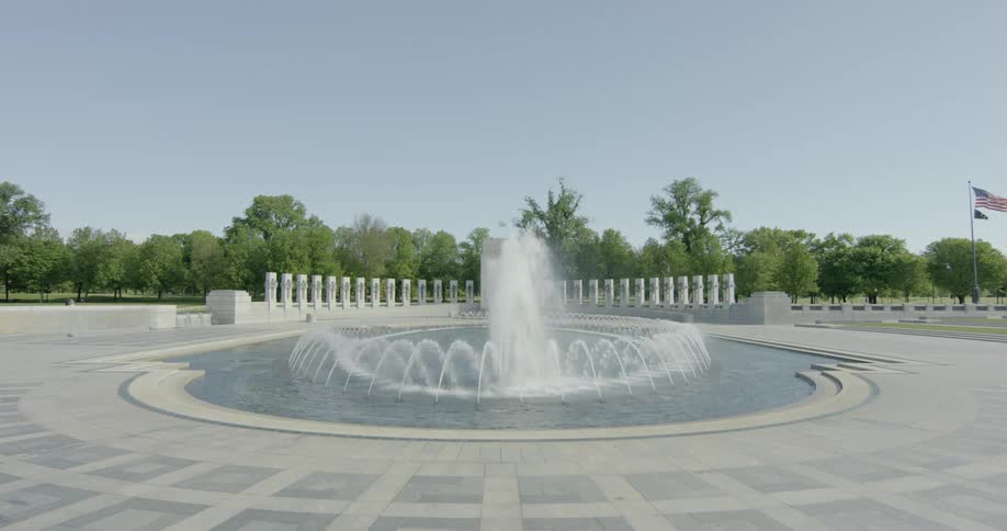 A fountain with water with trees and an american flag in the background