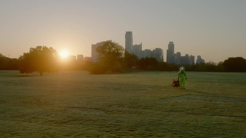 A man wearing protective gear and pulling a cart walks across a field