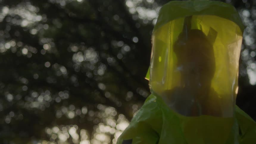 A man in a hazmat suit looking around while walking outdoors with the sun at his back