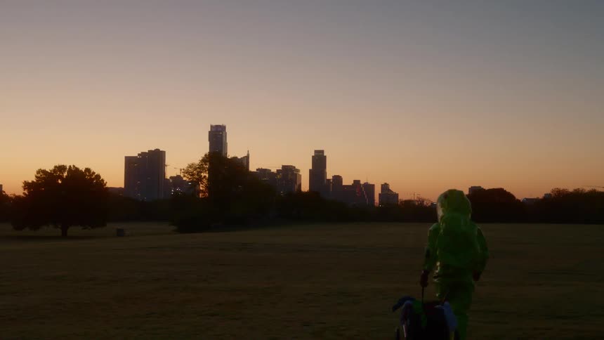 A person in a hazmat suit pulling a cart with a city skyline in the foreground
