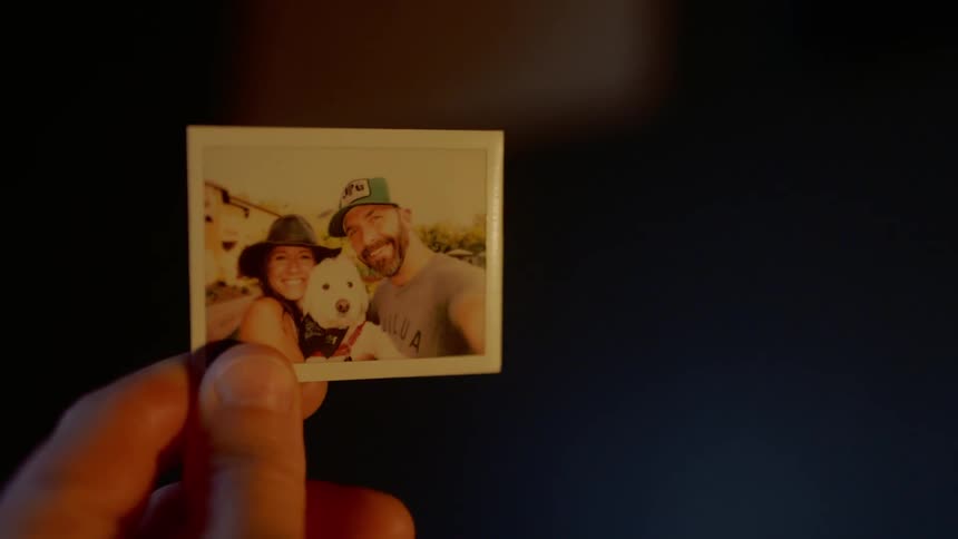 A man holds a photograph of a man woman and dog