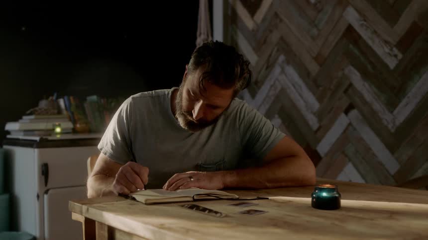 A man sits at a table and writes in a book