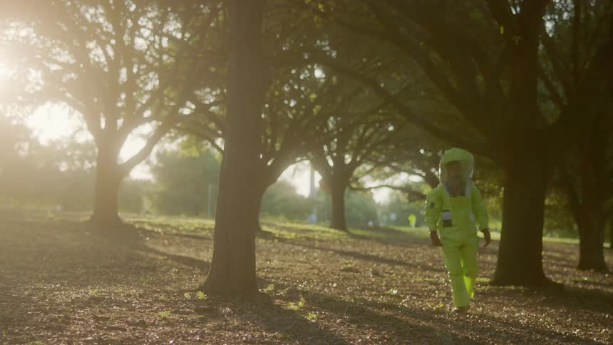 A person walks in a park area wearing a hazmat suit