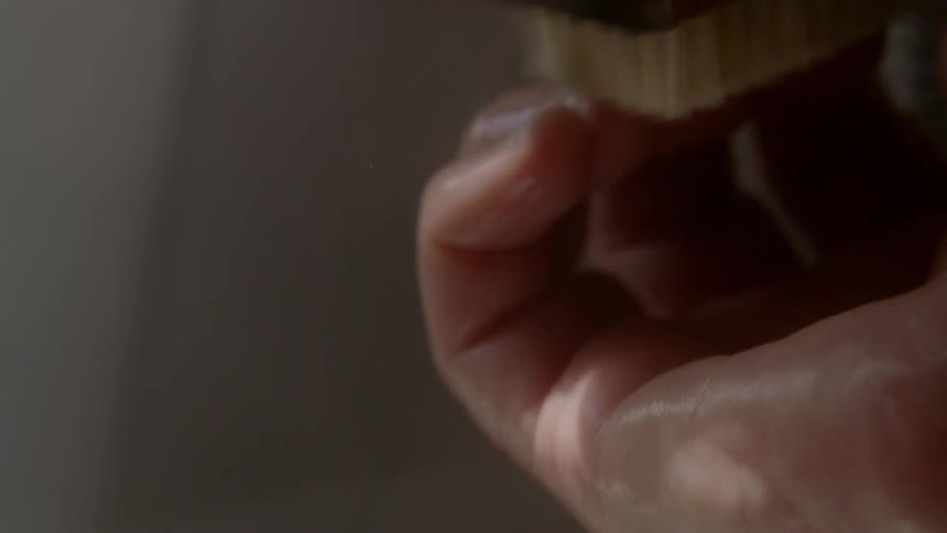 A person uses a brush to thoroughly scrub their fingers and nails in a shower