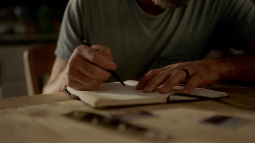 A man sits down and starts to write in a book