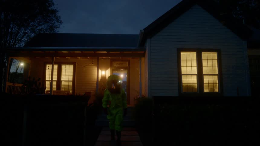 A person walks out of a house in a hazmat suit