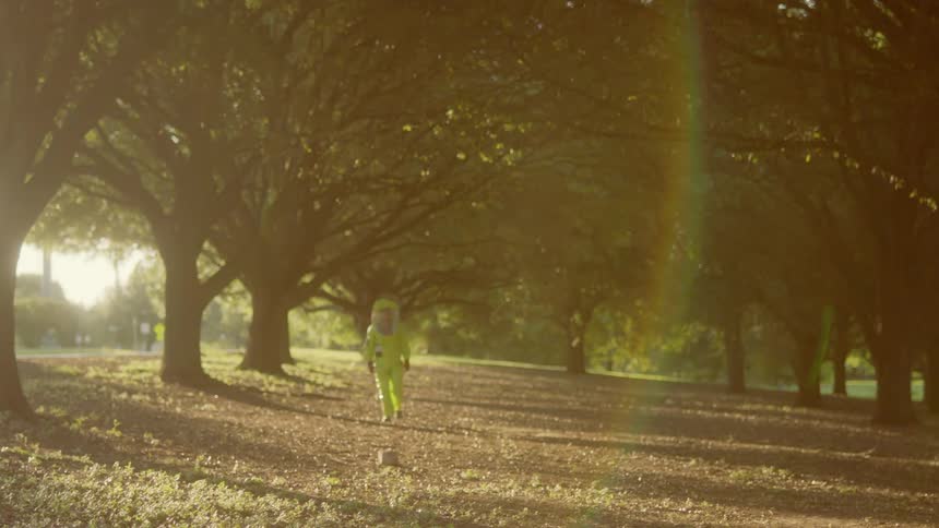 Person wearing personal protective gear walks through fallen leaves under trees