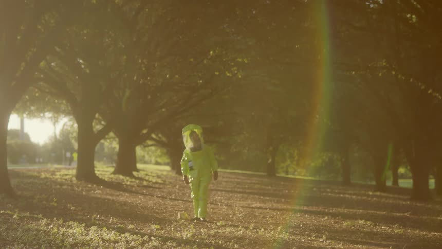 A person in a protective suit is in a grassland area with trees