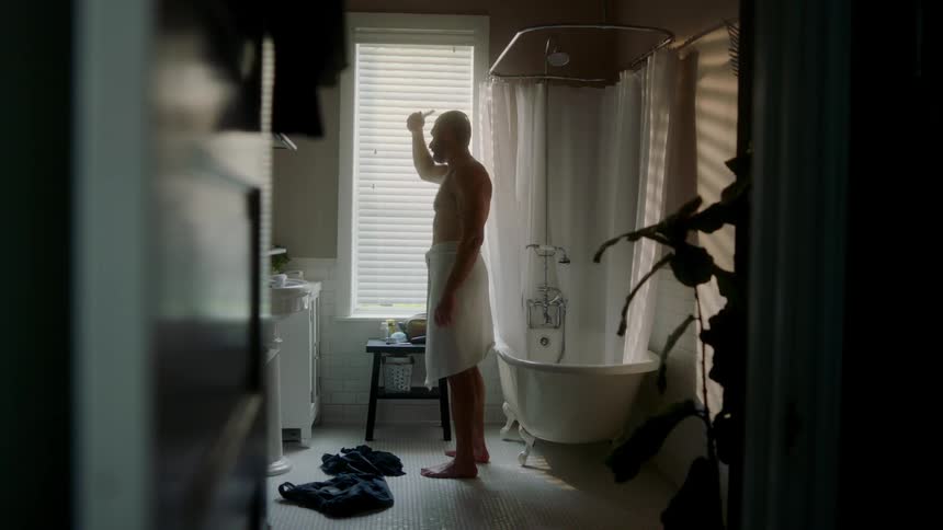 A man stands in his bathroom and combs his hair