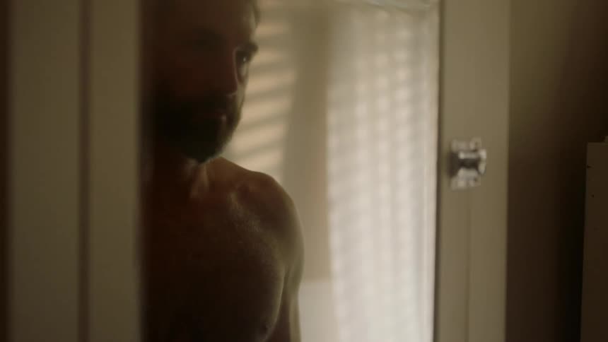 A man walks towards a mirror and looks at himself