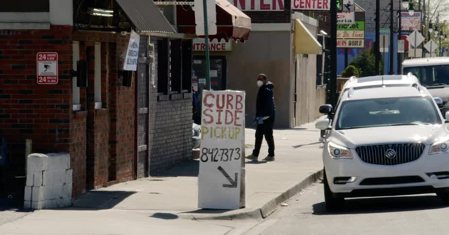 A man with a mask and disposable gloves walking on the sidewalk curbside pickup
