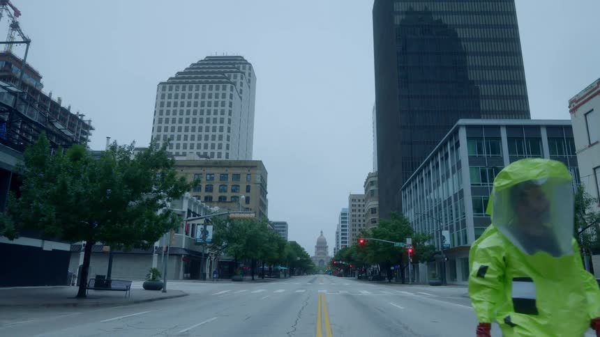 A man walking with a hazmat suit on a city street with buildings in the background