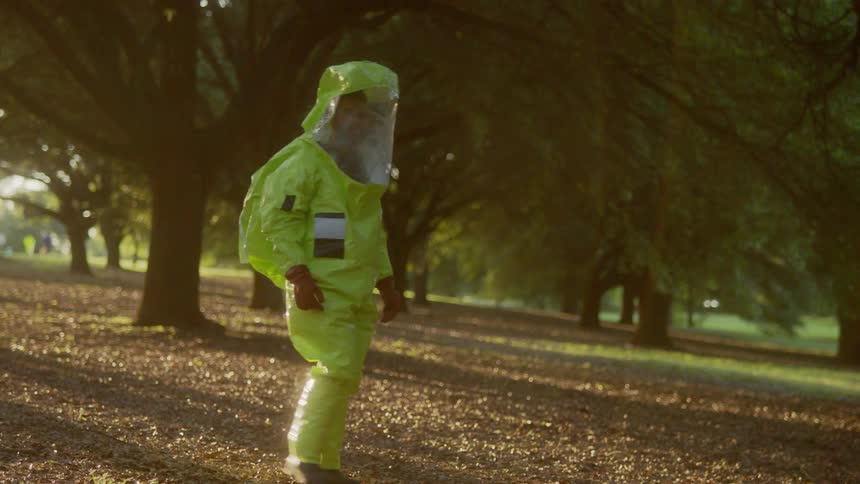 A man in a hazmat suit walking through a grove gazing around himself