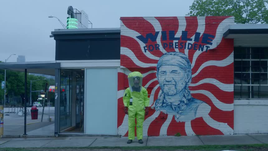 A man wearing protective gear stands in front of a mural of willie nelson