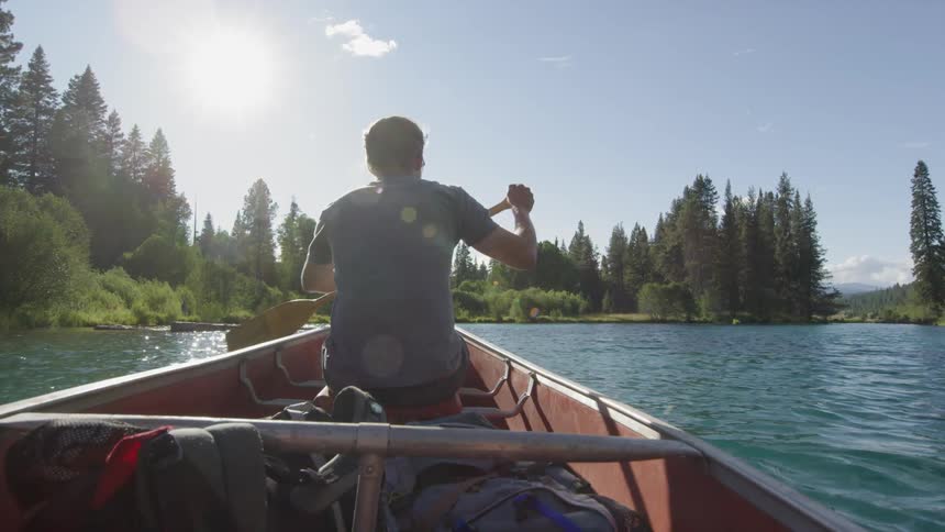 A man paddles a boat down a river on a sunny day
