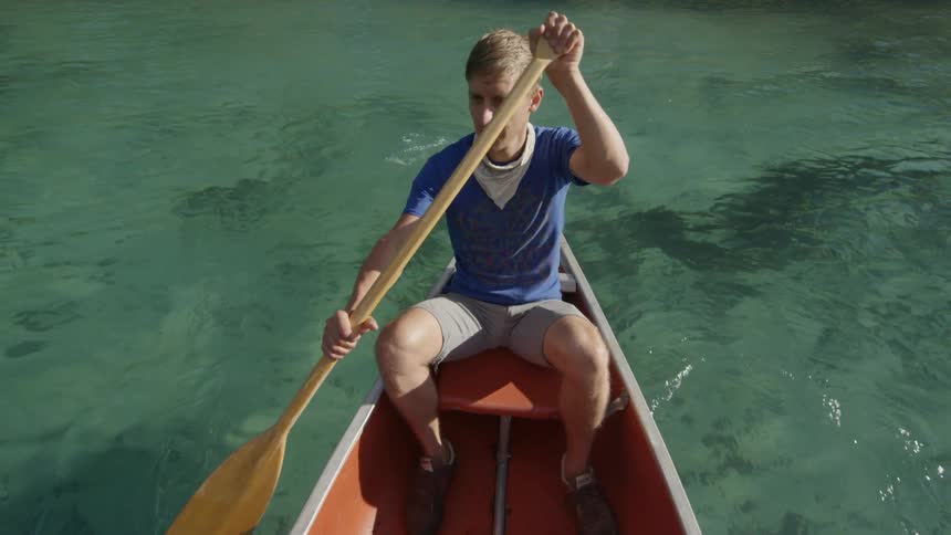 A man paddles a canoe on a sunny day