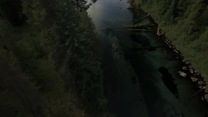 A rowboat floats down a river in the woods