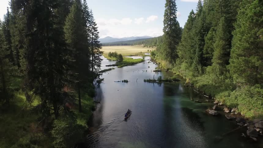Two people paddle a kayak down a river through a forest