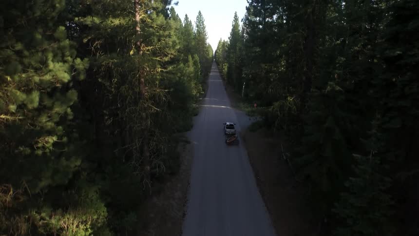 A truck is driving down a small road between two forest ranges