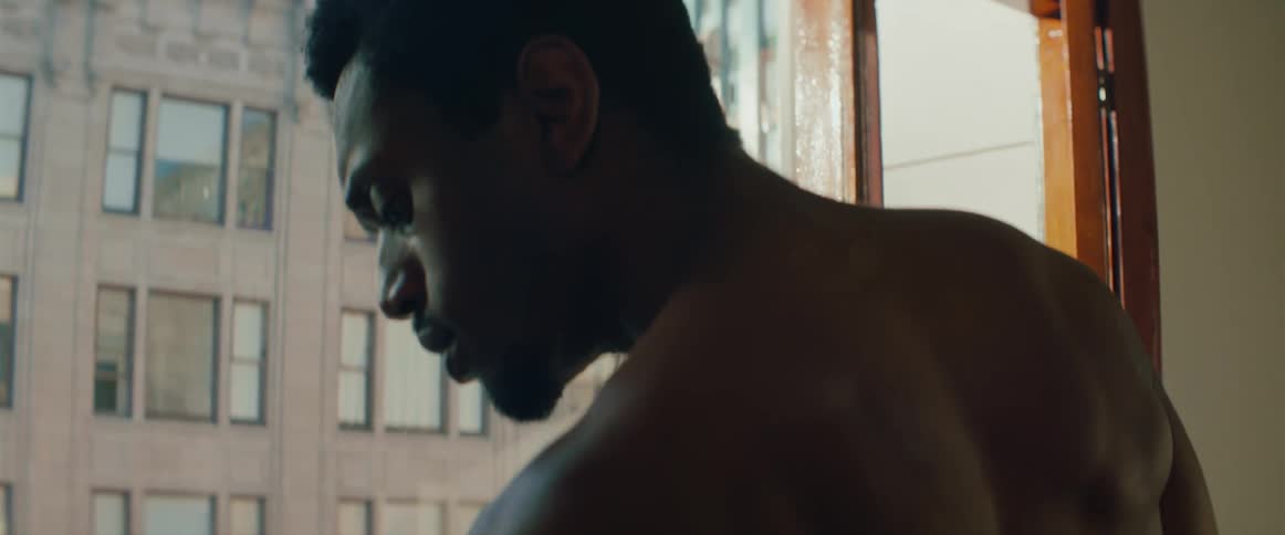 A man standing next to a window then looking down at his hand