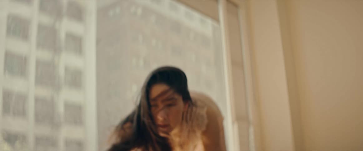 A woman in a nightgown twirls and dances in front of a large window then goes down to her hands and knees