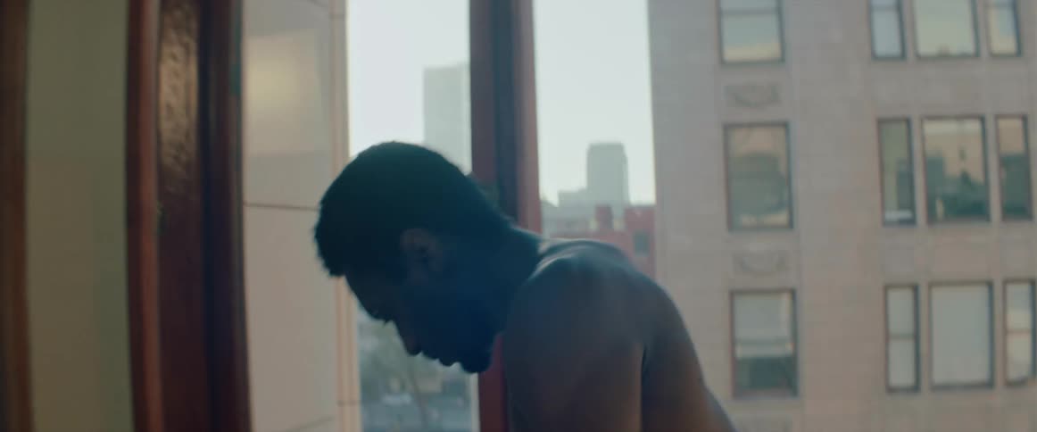 A man performs a modern dance in front of a large window with views of downtown