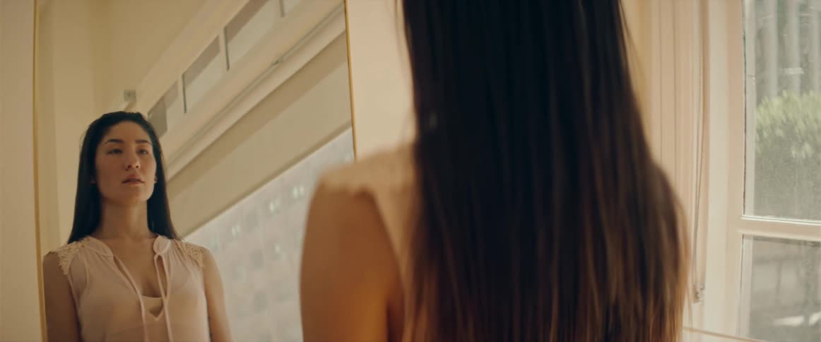 A woman walks towards a mirror and then looks at herself