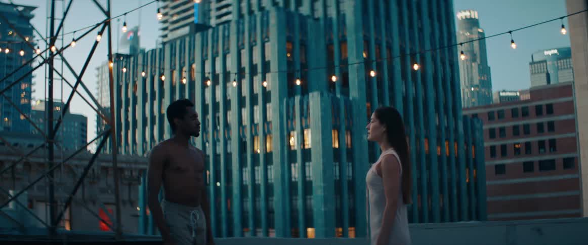 Man and woman approach each other just after dusk with skyscrapers in background