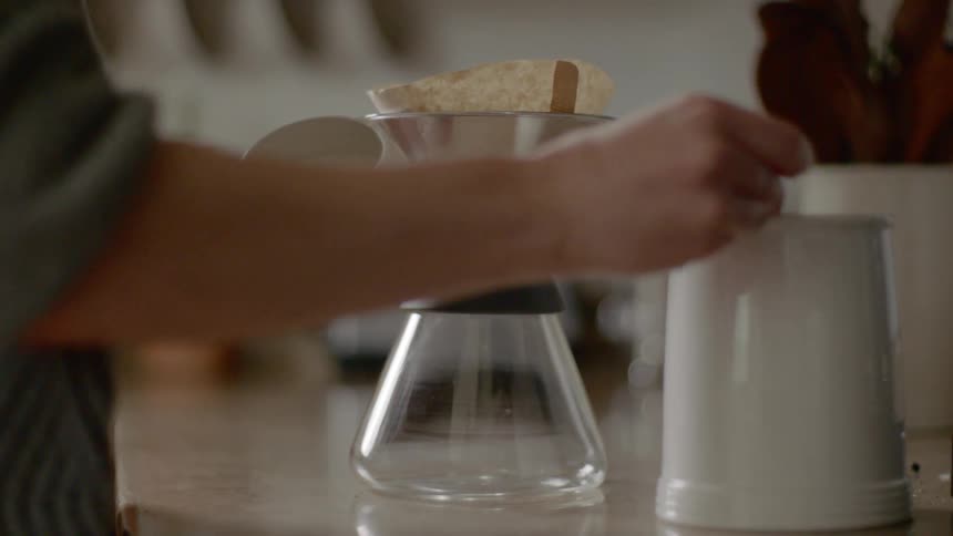 A person using a silver scoop to place coffee grounds into a filter