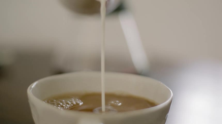 A woman pours cream in to a cup of coffee