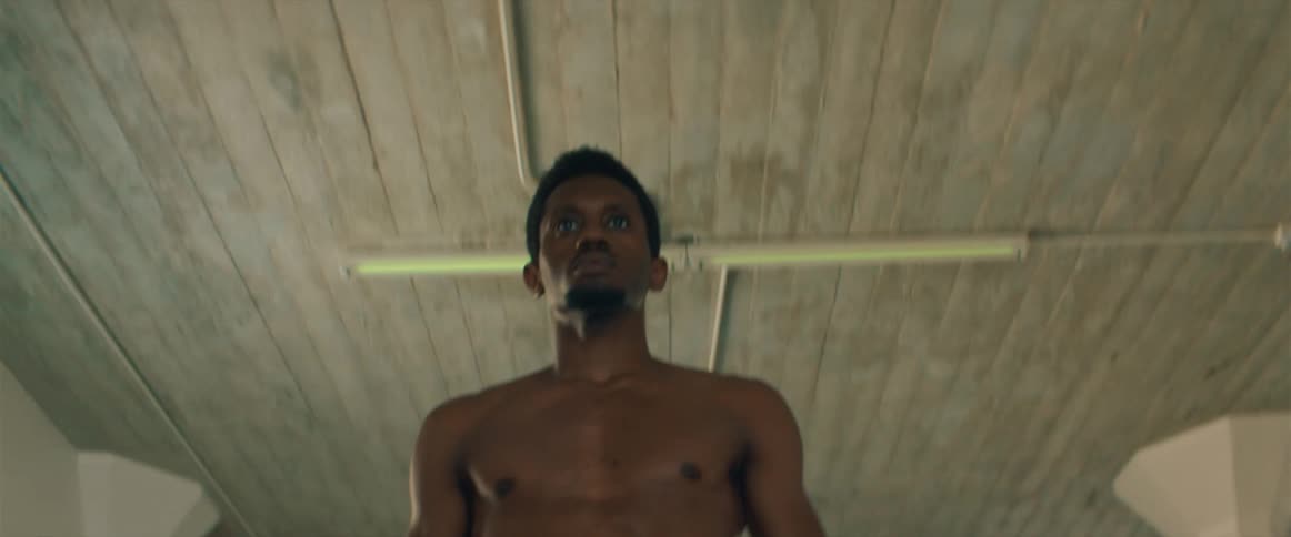 A man walking shirtless with lights flickering above him