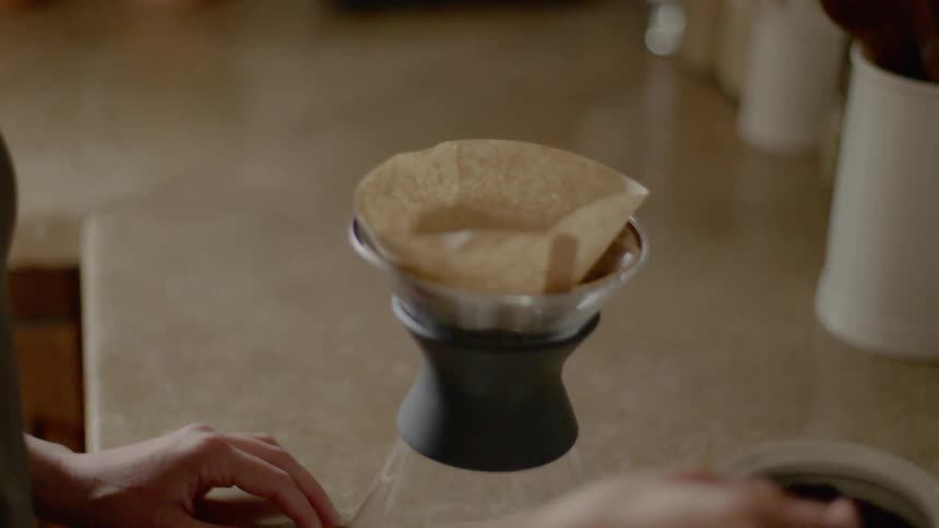 A persons hand taking coffee grounds with a silver scoop and placing it in a filter