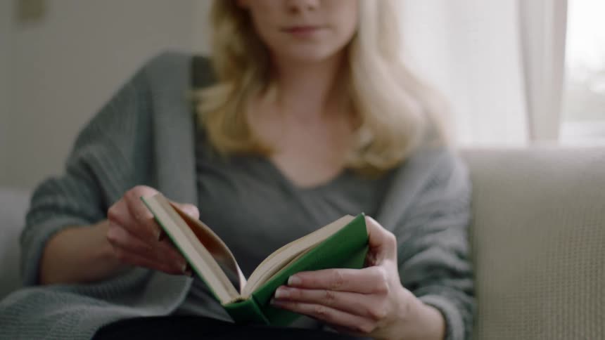 A woman sits on a couch and opens a book