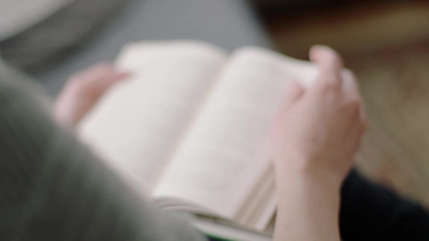 A woman sits reading a book she is holding in her lap