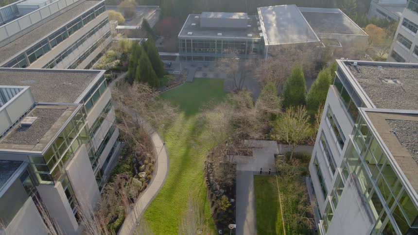 Pullback reveal of trees, grass and paths along a courtyard between low rise office buildings