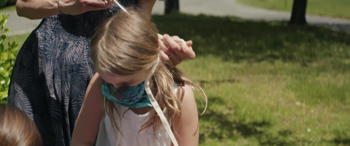 Mother tying face mask on daughter outdoors on the lawn