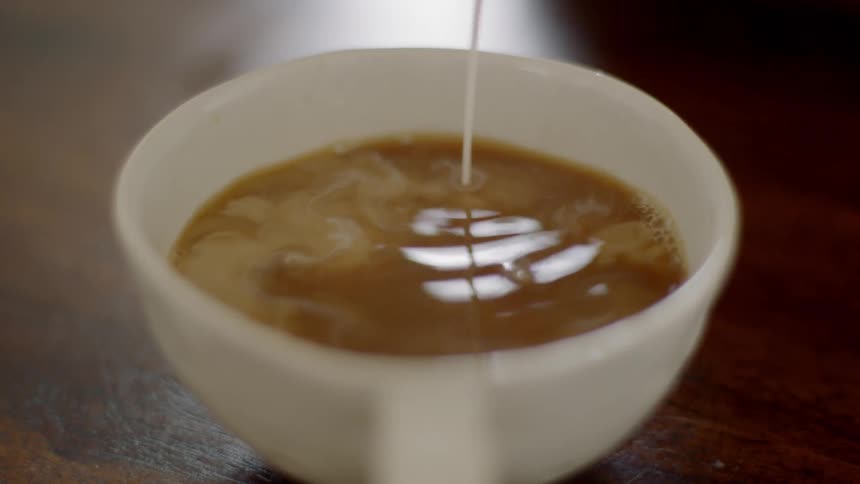 Milk pouring in coffee in a small white mug