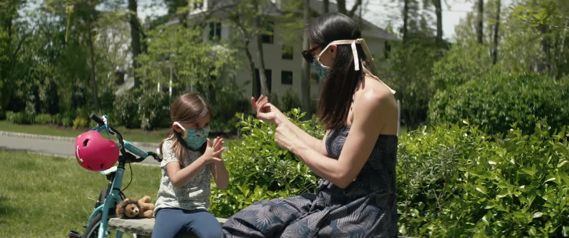 Mother and daughter wearing face masks sitting on bench playing